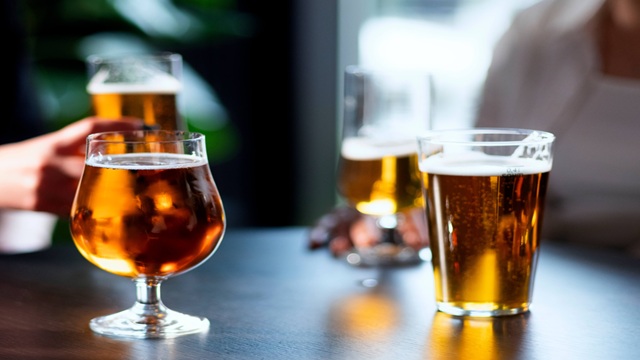 Four glasses of beer on a dark table, showing different beer styles with golden and amber colors in a casual indoor setting.